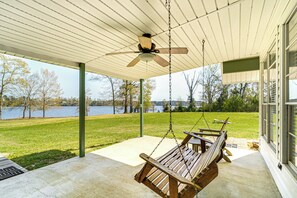 A covered porch with a swing chair, a ceiling fan, and a view of a lake.