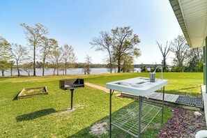 An outdoor patio with a grill, a sink, and a small deck area overlooking a lake.