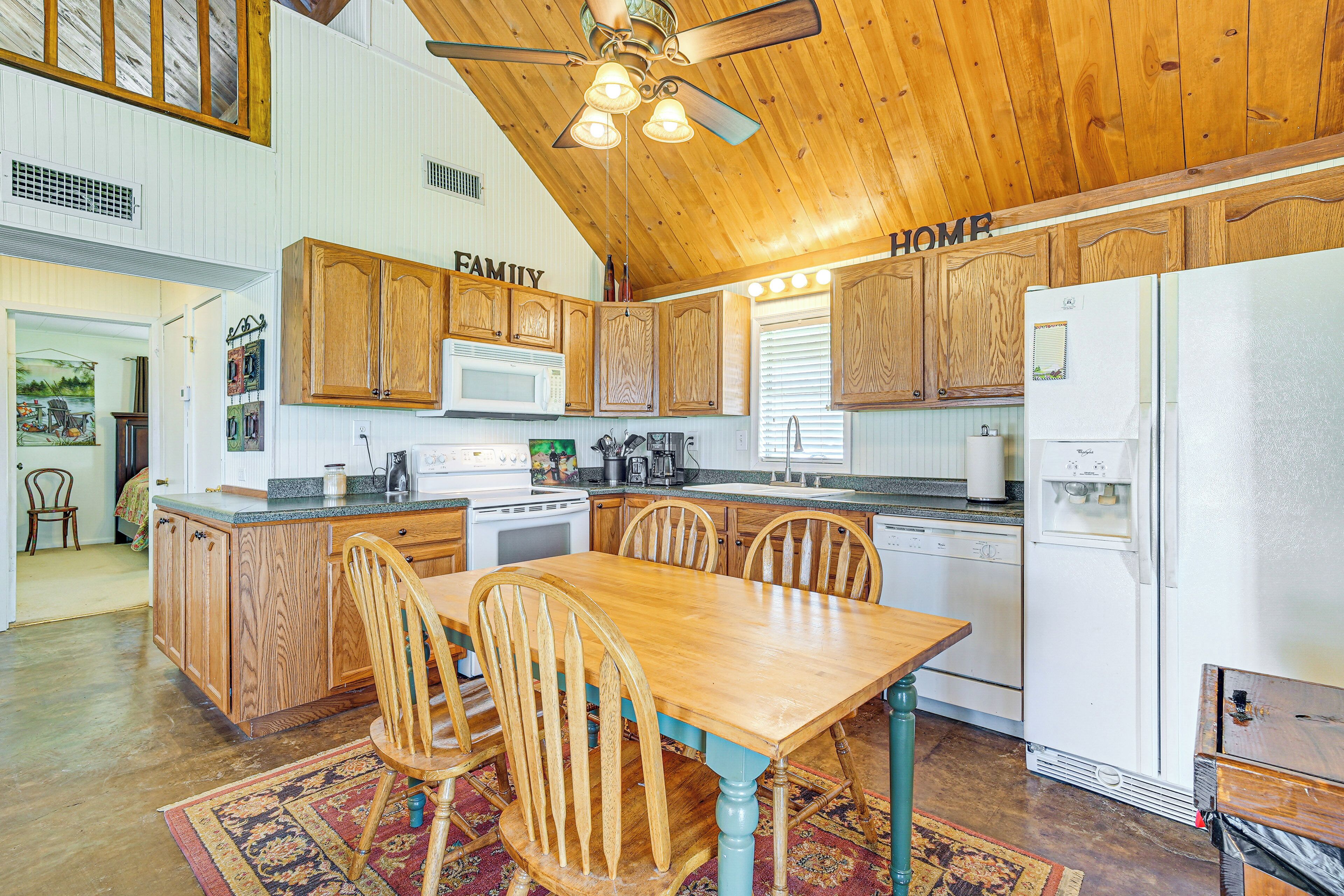 A kitchen with wooden cabinets, a dining table, chairs, a refrigerator, and a ceiling fan.