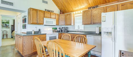 A kitchen with wooden cabinets, a dining table, chairs, a refrigerator, and a ceiling fan.