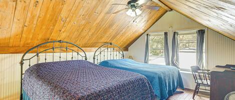 Une chambre avec deux lits, un ventilateur de plafond, un bureau et une fenêtre avec des rideaux.