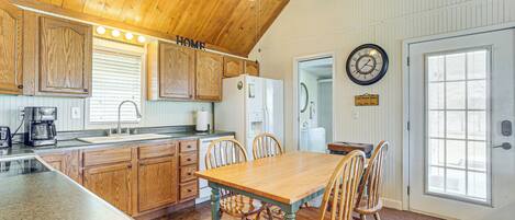 A kitchen with wooden cabinets, a granite countertop, a dining table with chairs, a ceiling fan, and a clock on the wall.