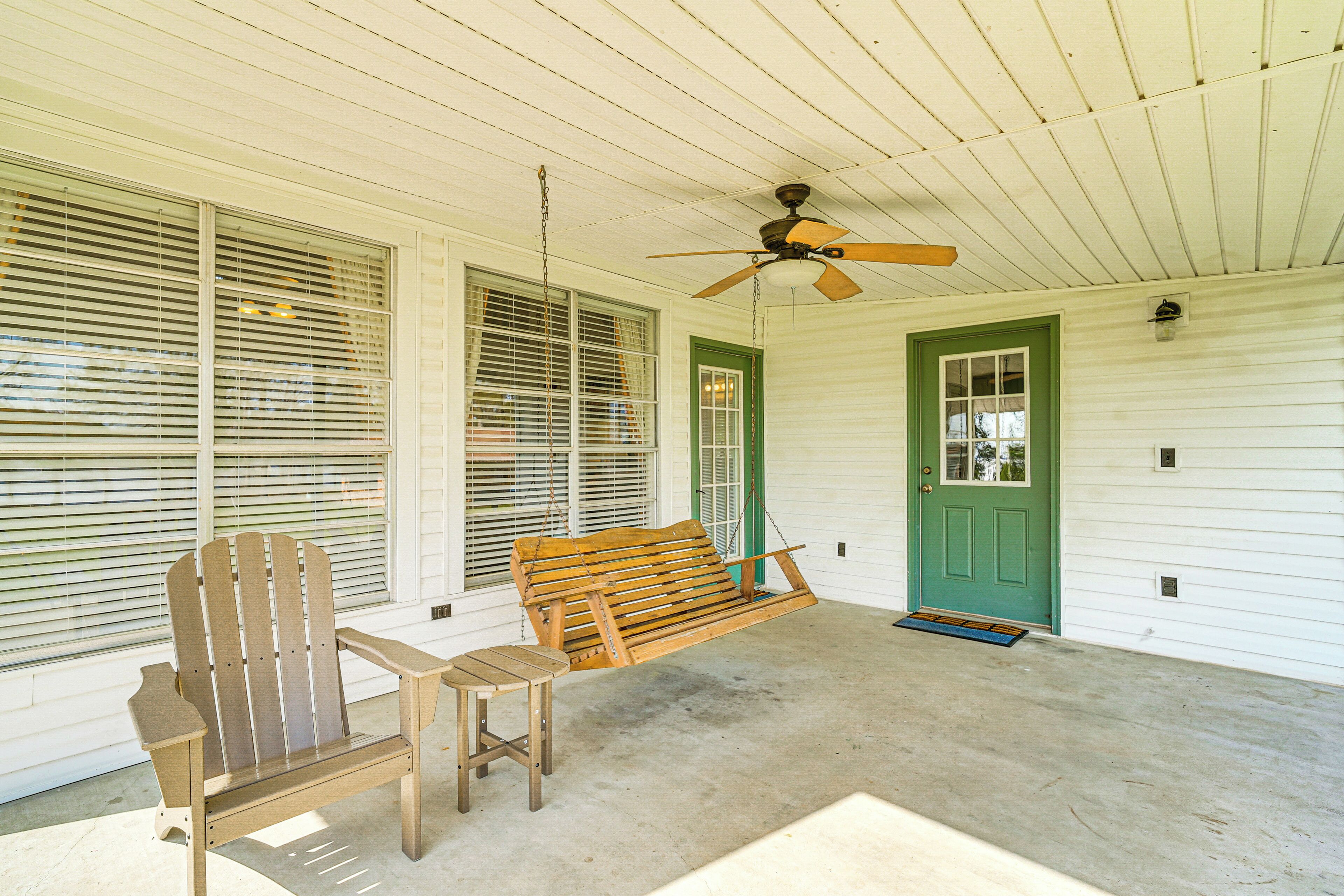 A porch with a wooden swing, a rocking chair, and a ceiling fan.