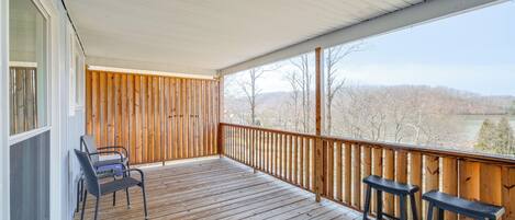 Una terraza de madera con dos taburetes de bar y una silla, con vistas a un paisaje pintoresco.