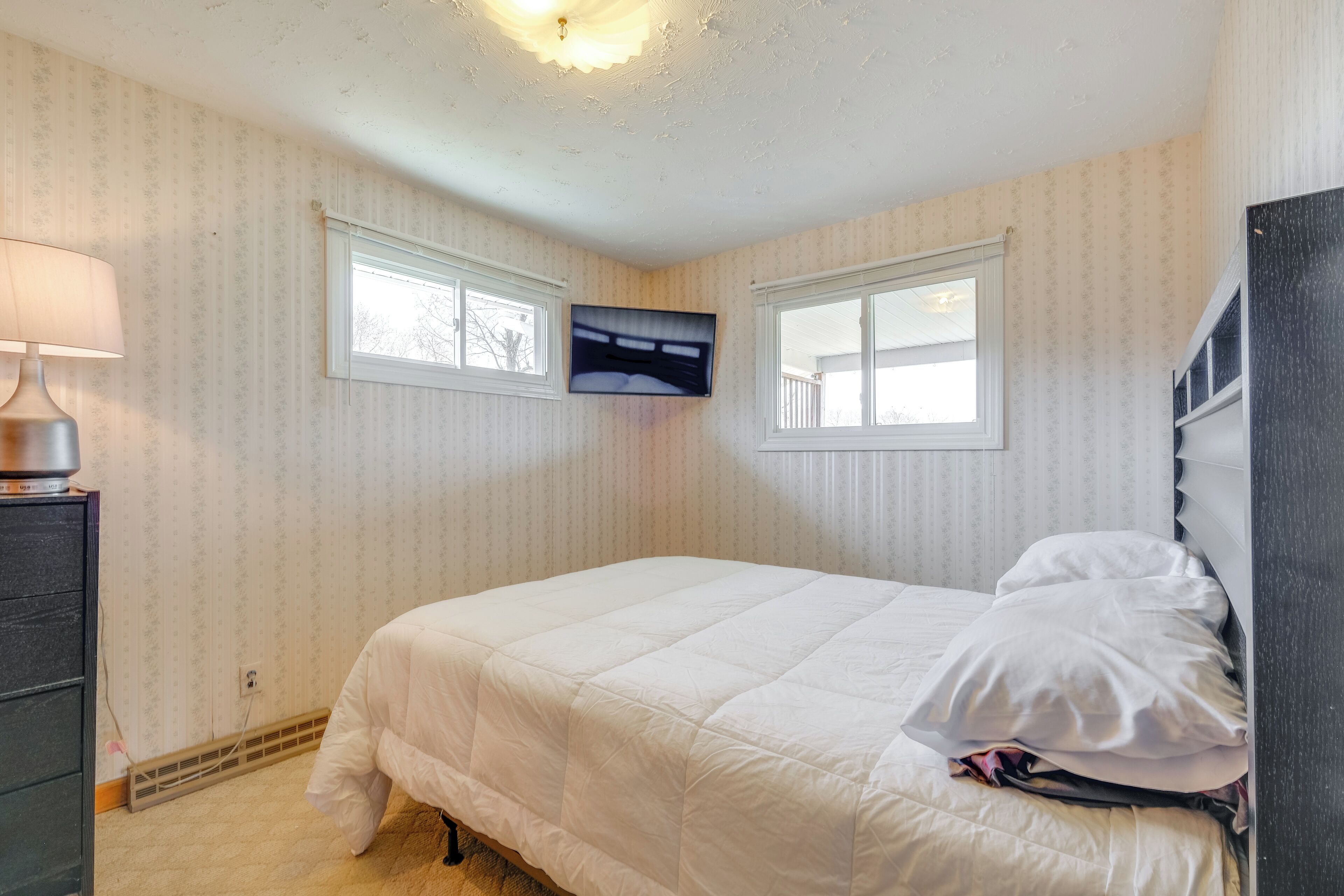 A bedroom with a bed, a TV mounted on the wall, and a dresser.