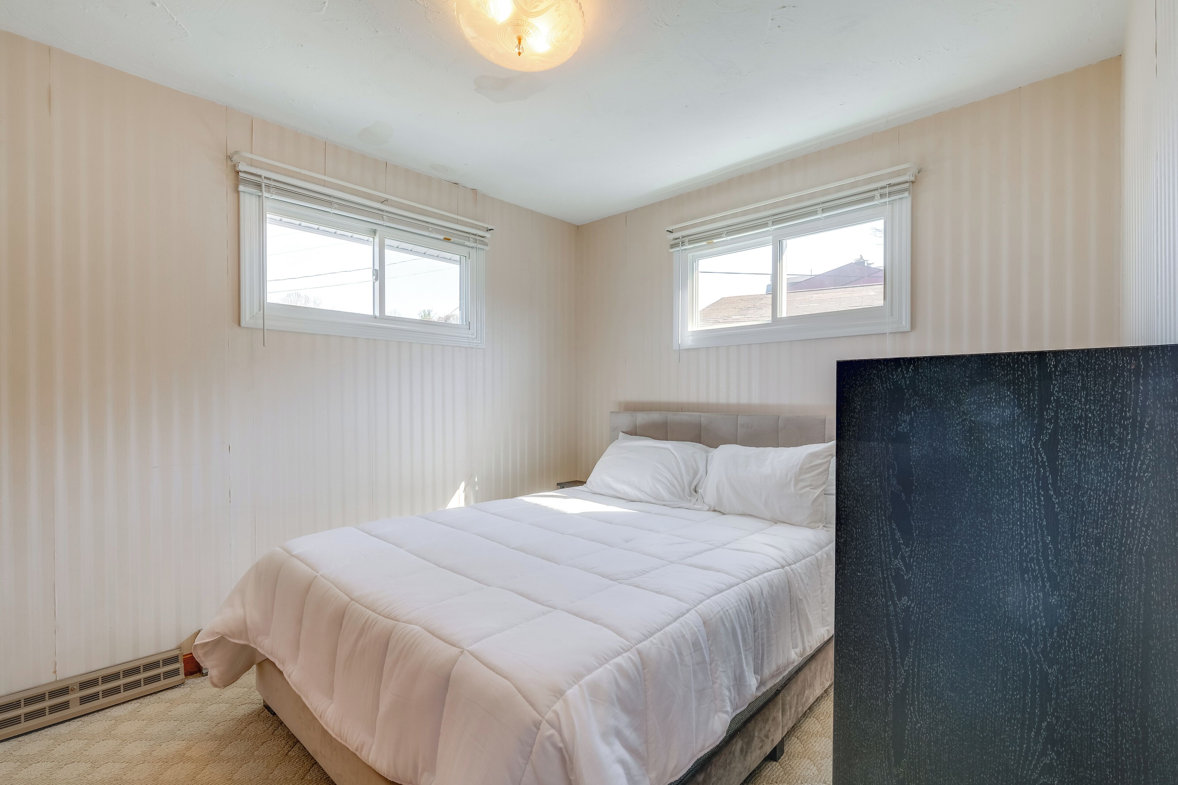 Une chambre à coucher avec un lit, deux fenêtres, un radiateur et une grande œuvre d’art noire accrochée au mur.