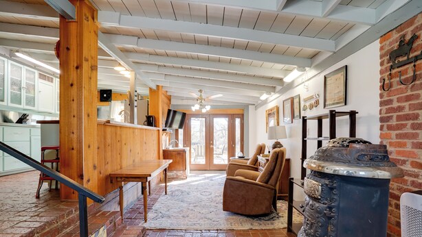 Un intérieur rustique avec un escalier en bois, une cheminée en pierre et un coin cuisine doté de meubles blancs et d’un comptoir en bois.