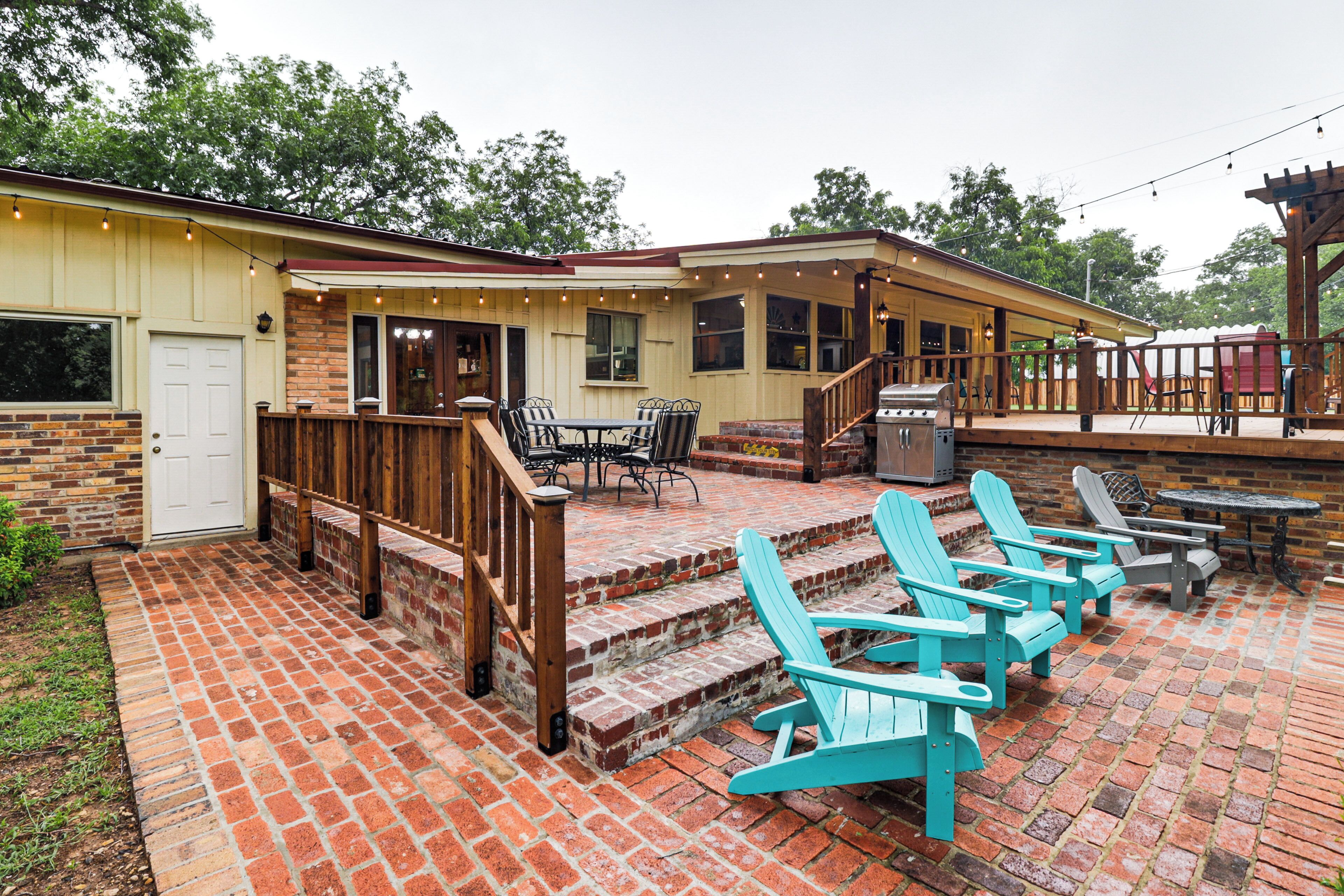 Un patio couvert avec un sol en briques, un espace extérieur aménagé avec des chaises et des tables, et un barbecue.
