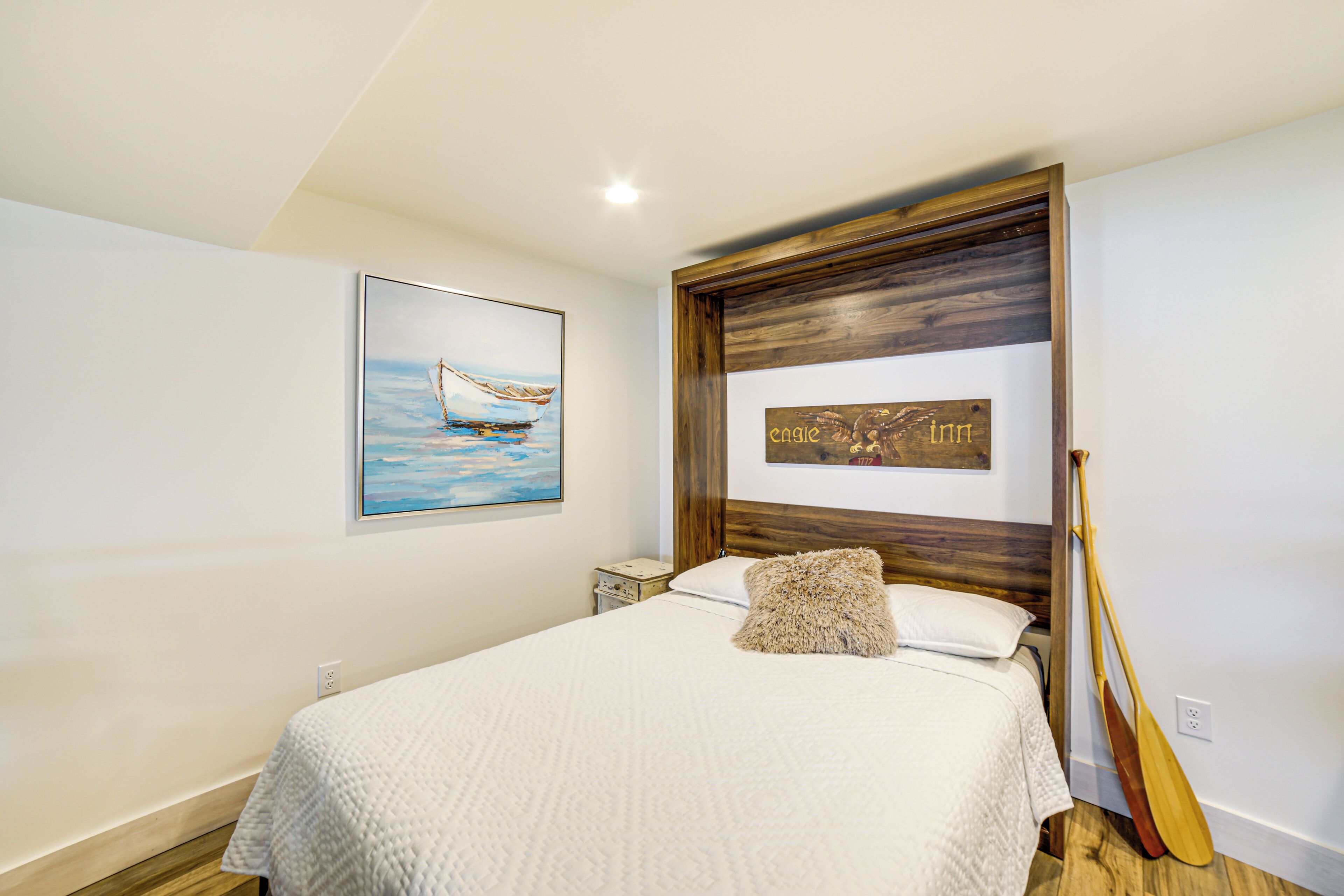 A bedroom with a bed, a painting of a sailboat, a wooden headboard, and a sign that says "Eagle Inn".