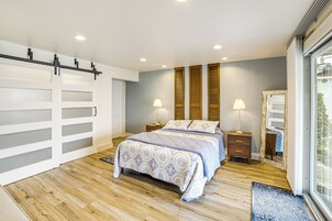 Un dormitorio con una cama, dos mesitas de noche con lámparas, un ventanal grande y una puerta corredera.