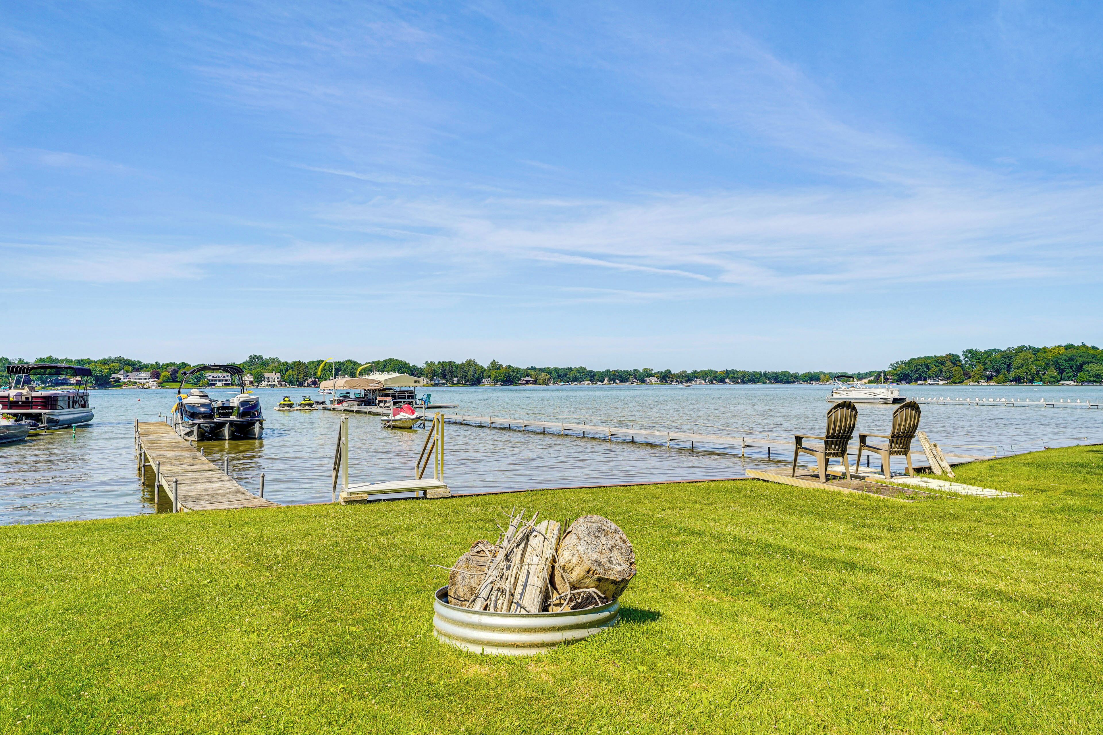 A lakeside dock with boats, a grassy area, and a row of chairs facing the water.