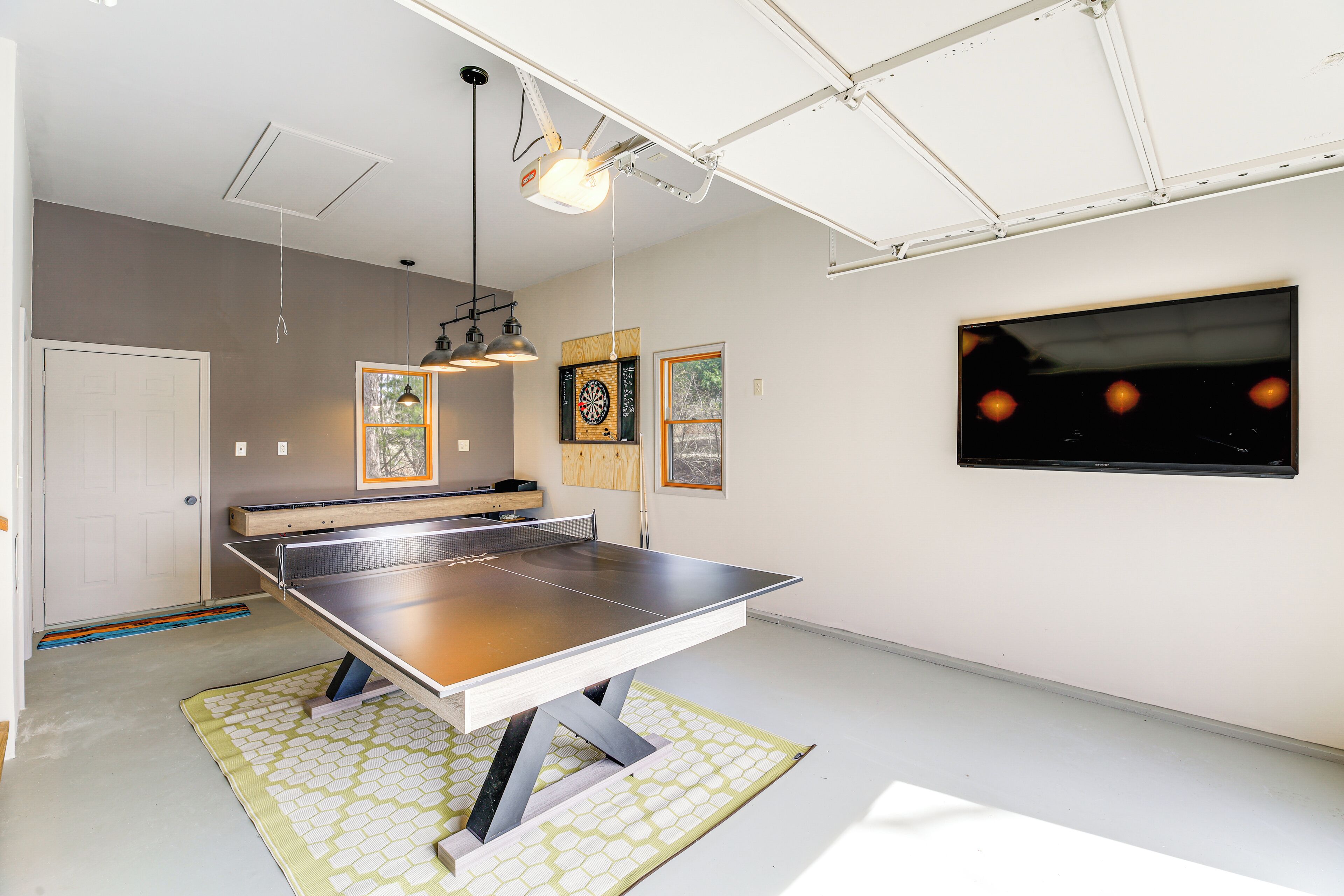 A ping pong table in a room with a white ceiling, a dartboard, and a framed picture on the wall.