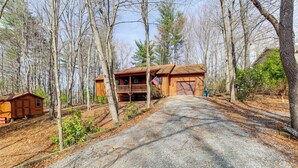 A cabin with a wooden deck and an American flag, surrounded by trees. - Deer River Retreat: Cabin Feel w/ Modern Touches (Sparta)