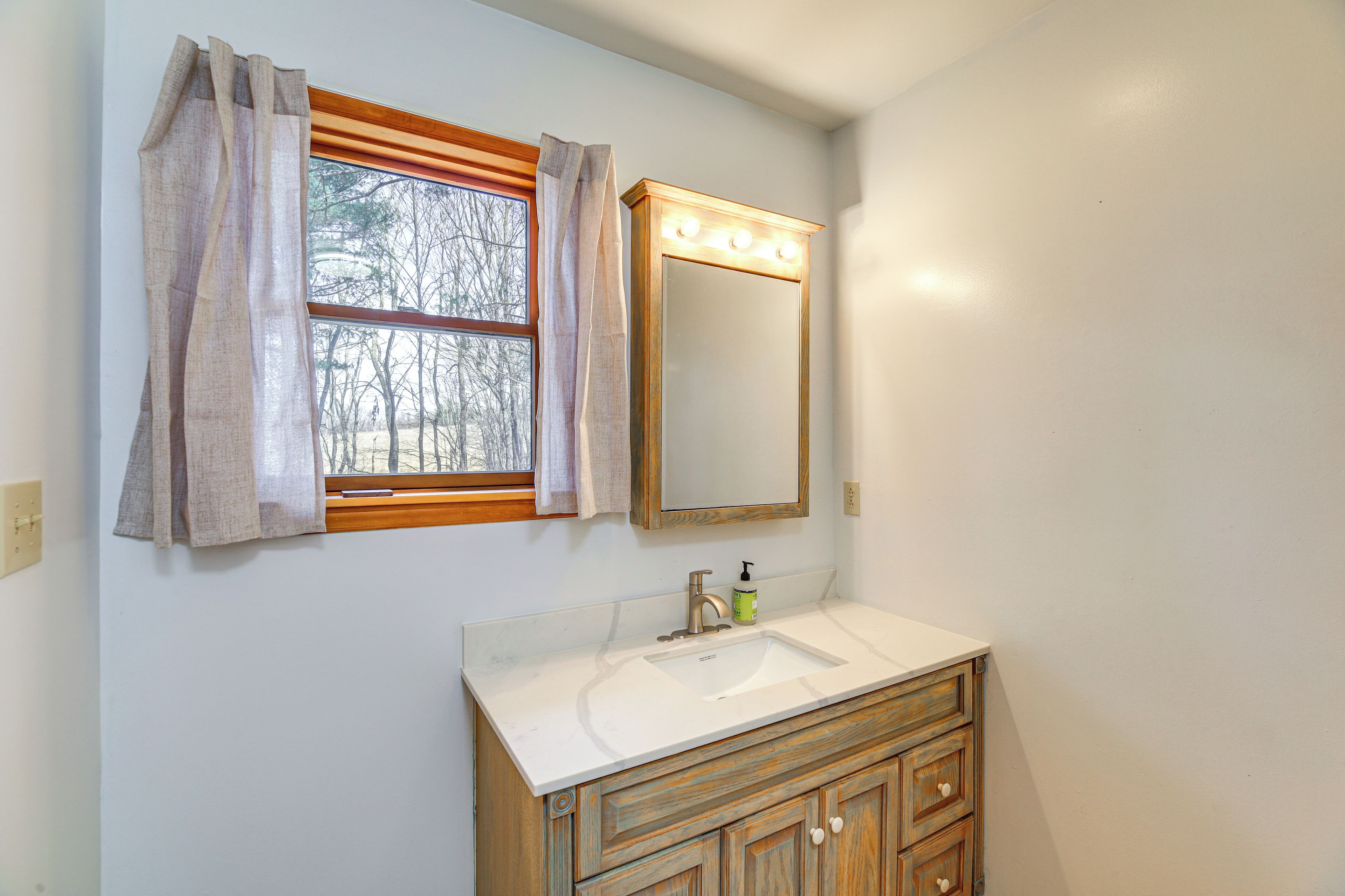 A bathroom with a window, vanity, and mirror.