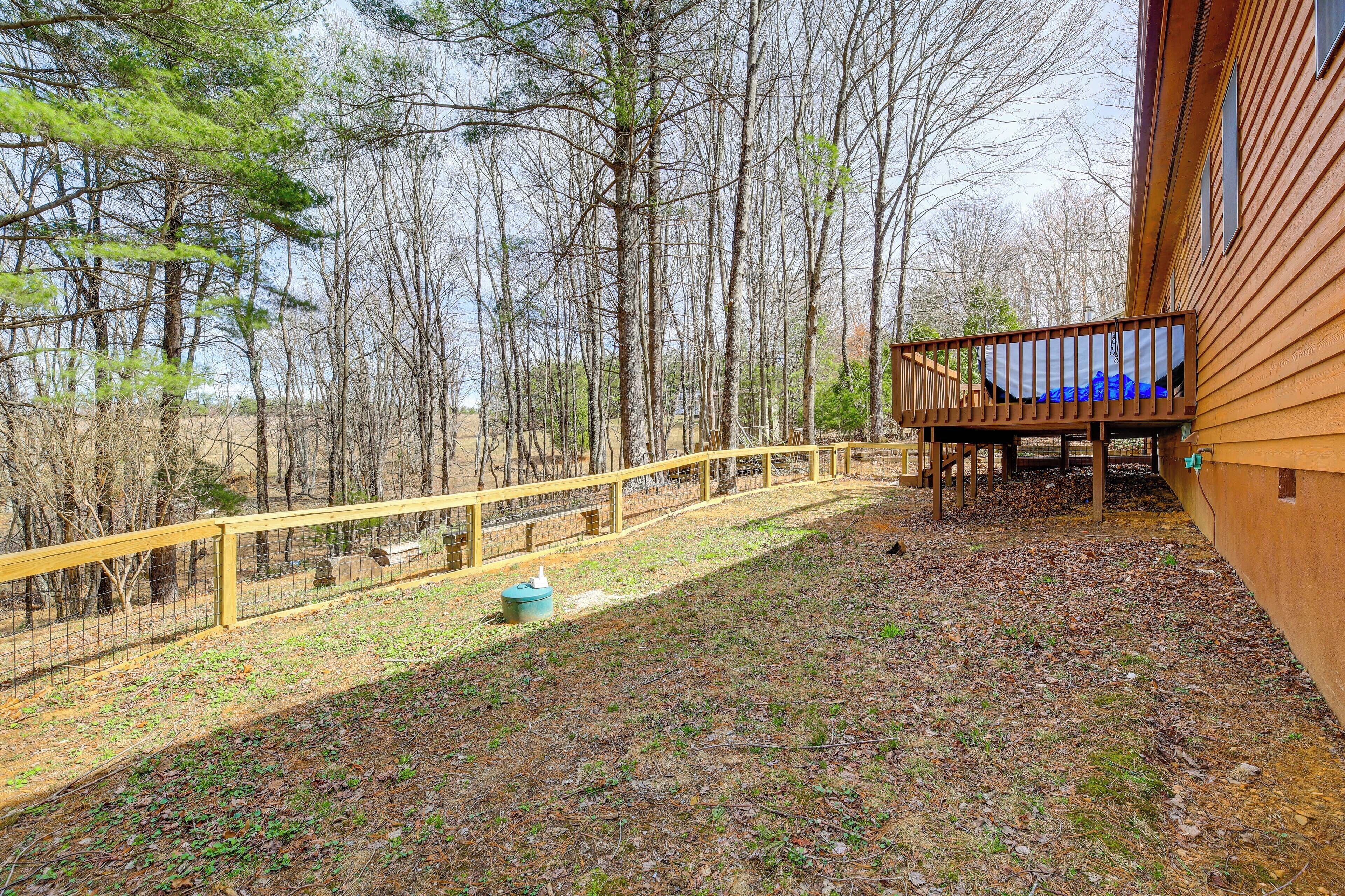 A wooden deck with a railing, surrounded by trees and a fenced area.