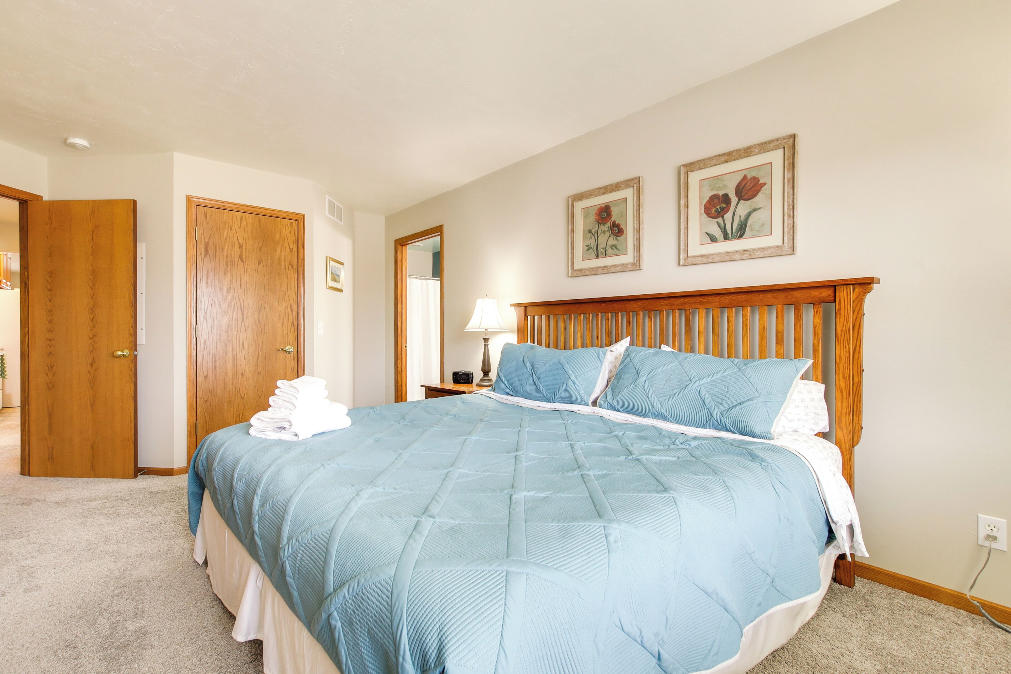 Un dormitorio con una cama grande, cabecera de madera y dos cuadros enmarcados con motivos florales en la pared.