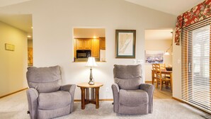 A living room with two grey armchairs, a small wooden table with a lamp, a framed map on the wall, and a dining area visible through an open doorway. - 'rise and Shine in Door County!' Egg Harbor Haven (Egg Harbor)
