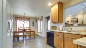 A kitchen with wooden cabinets, a dishwasher, a dining table with chairs, and a window with plaid curtains. - 'rise and Shine in Door County!' Egg Harbor Haven (Egg Harbor)