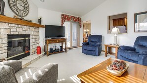 A living room with a stone fireplace, a television, a blue armchair, and a wooden coffee table. - 'pattie's Other Place' - Indoor Pool Access! (Egg Harbor)