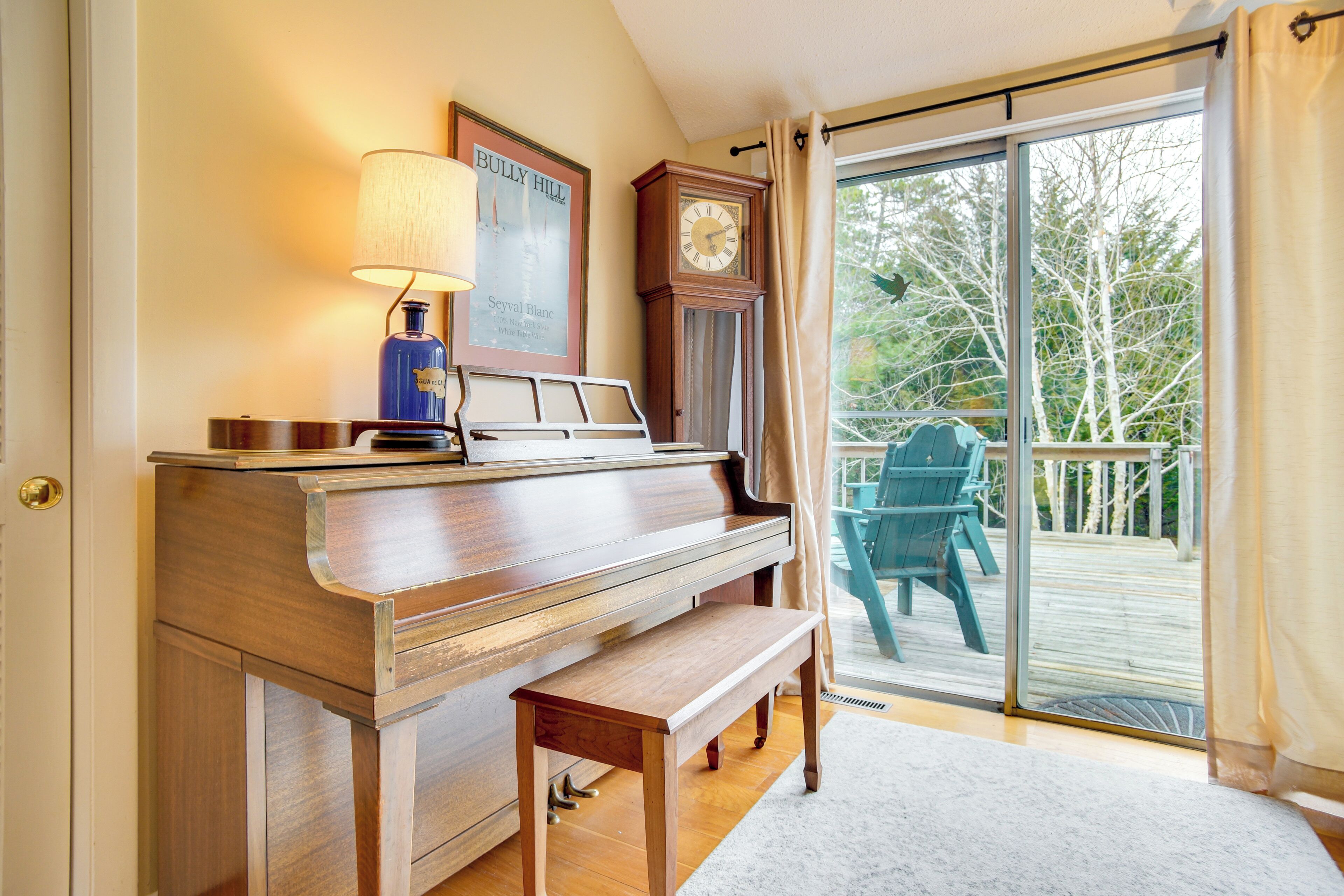 A piano in a room with a large window and a view of a deck.