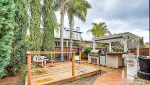 A backyard with a wooden deck, outdoor seating, a barbecue area, and a pergola.