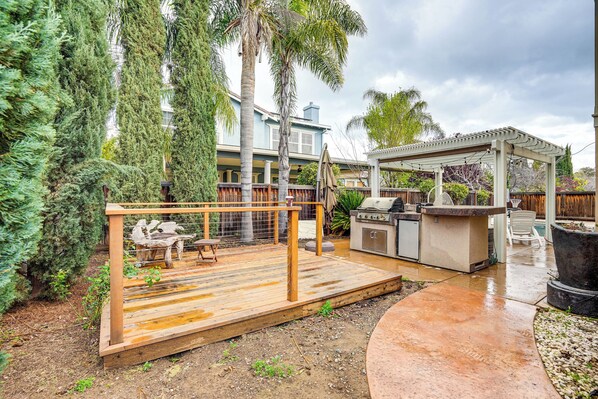 A backyard with a wooden deck, outdoor seating, a barbecue area, and a pergola.