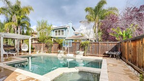 A backyard with a swimming pool, a wooden deck, and a house with a blue exterior.