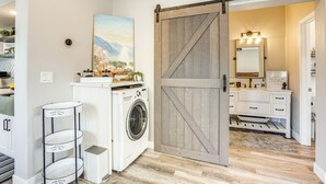A laundry area with a washing machine, a drying rack, and a painting on the wall.