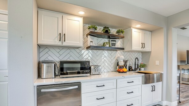 A modern kitchen with white cabinetry, stainless steel appliances, and a herringbone tile backsplash.