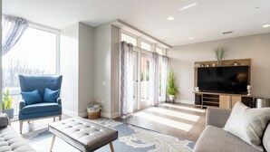 Ein modernes Wohnzimmer mit einem blauen Sessel, einem grauen Sofa, einem großen Flachbildfernseher und einer Holz-Unterhaltungseinheit.