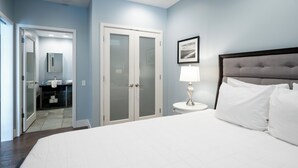 Ein Hotelzimmer mit einem großen Bett, einem Nachttisch mit Lampe, einem Kleiderschrank und einem durch eine offene Tür einsehbaren Badezimmer.