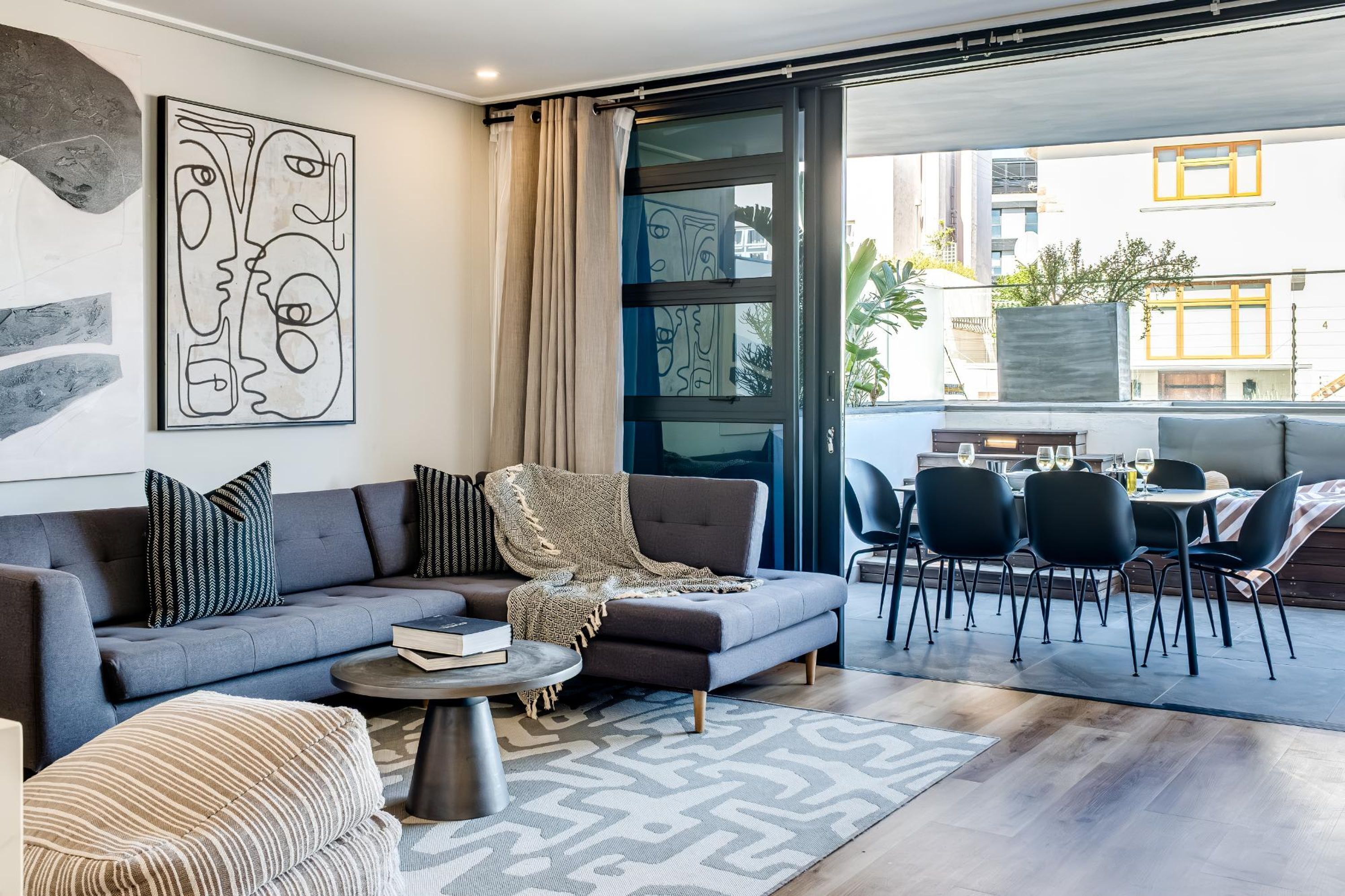 A modern living room with a grey sofa, a coffee table, and a dining area with chairs and a table.