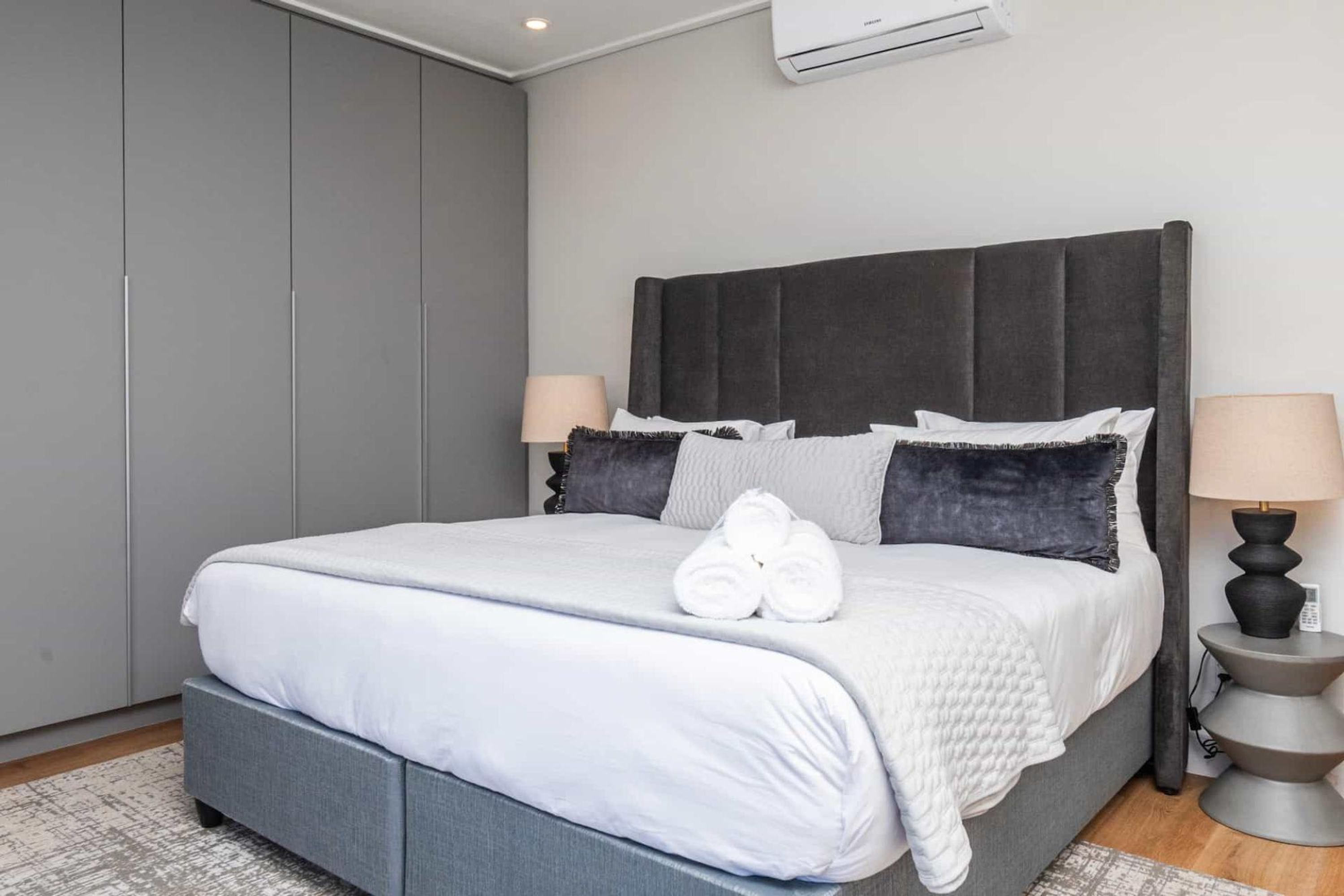 A modern bedroom with a large bed, grey wardrobe, and two bedside lamps.