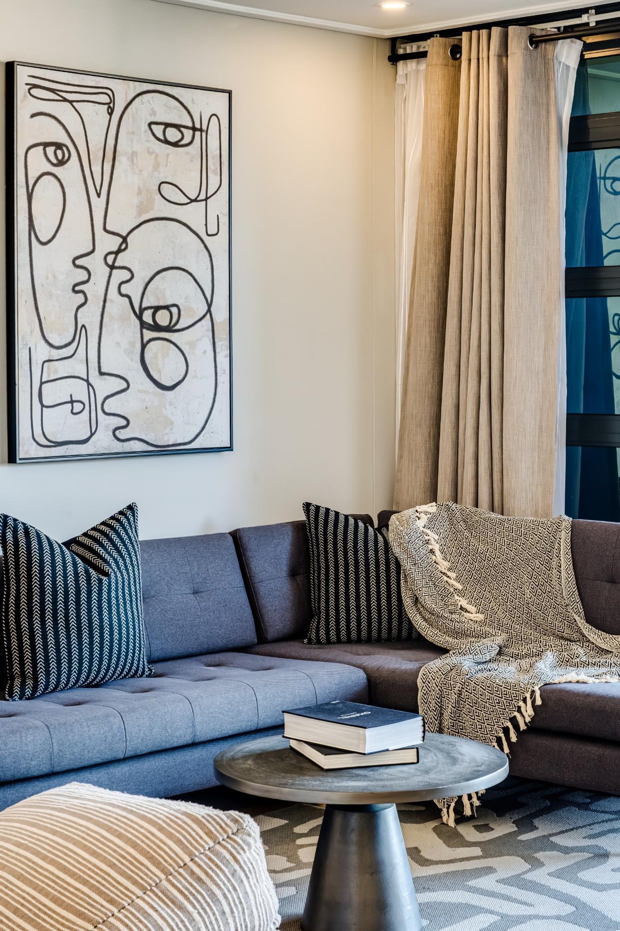 Un salon moderne avec un canapé gris, des coussins à motifs, une table basse ronde et une grande œuvre d’art abstraite accrochée au mur.