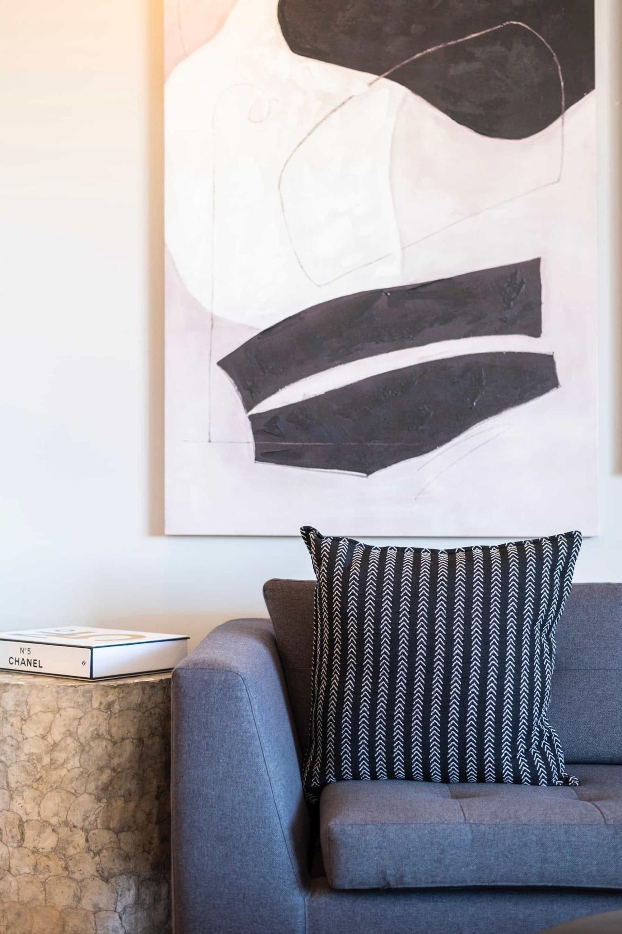 A modern living room with a grey sofa, a patterned throw pillow, and a large abstract painting on the wall.