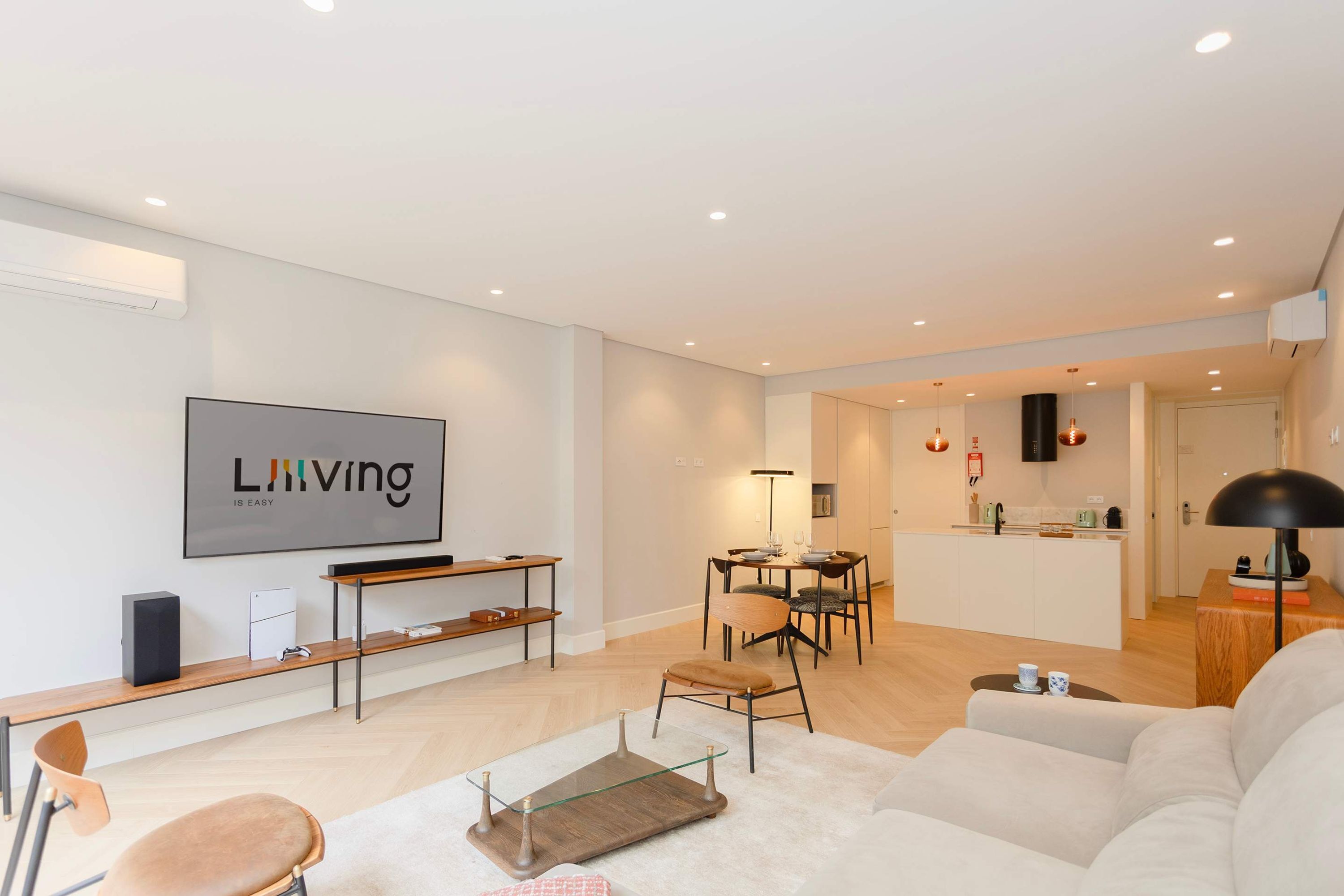 A modern living room with a flat-screen TV, a sofa, a coffee table, and a dining area with a table and chairs.