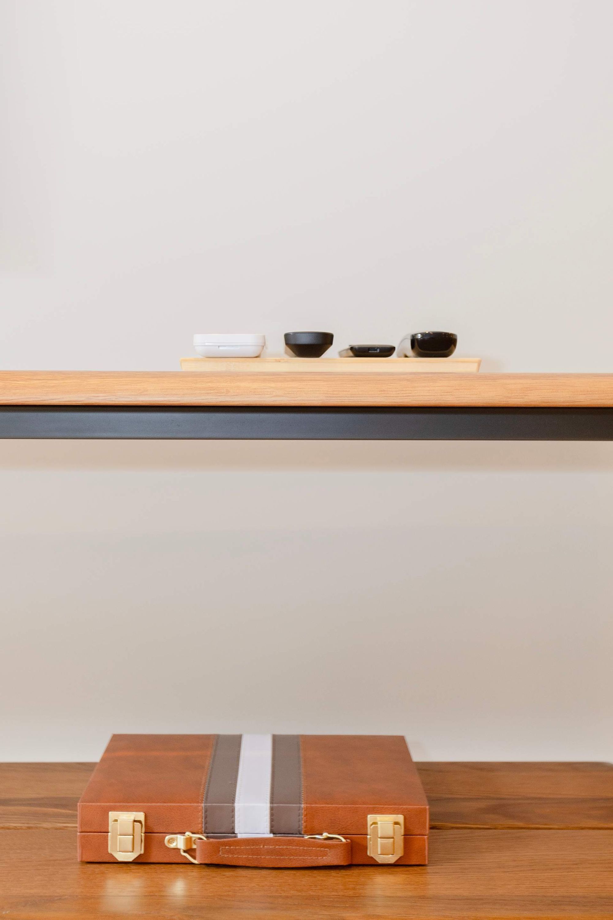 A wooden table with a brown suitcase and a shelf above it holding a white object and three black bowls.