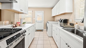 Een moderne keuken met witte kasten, een roestvrijstalen afzuigkap, een ingebouwde oven, een wasmachine en een spoelbak.