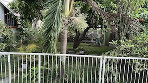 A lush garden with various plants and trees, a white fence, and a building with a window in the background. - Kingston Oasis - Private House With Mountain Views (Kingston)