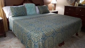 A bed with a patterned bedspread, a fluffy pillow, and a bedside table with a lamp.