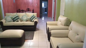 A living room with a sofa set, a coffee table, and a chair. There is a dining table with chairs in the background.