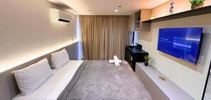 Una habitación de hotel moderna con una cama, un televisor de pantalla plana, un pequeño escritorio y una planta.