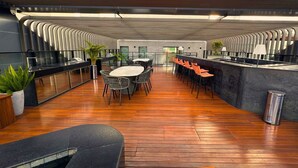 Een moderne binnenruimte met een houten vloer, een ronde tafel met stoelen in het midden, en een lange toonbank met krukjes.