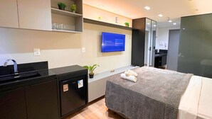 Een moderne hotelkamer met een bed, een bureau, een kleine koelkast, een televisie en een spiegel.