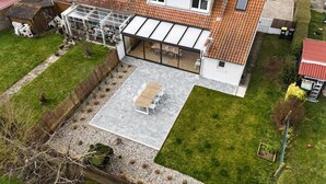 Luchtbeeld van een woonhuis met een terras, een tuinkamer en een omheinde tuin.