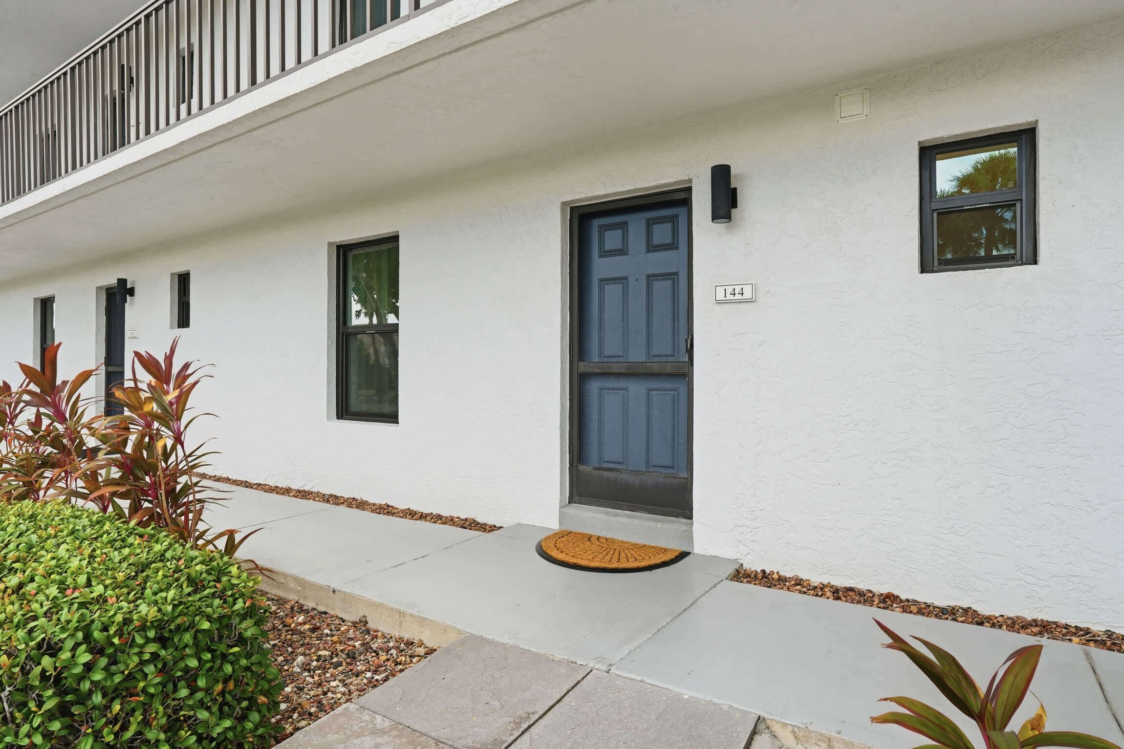 A white building with a blue door, numbered 144, and a small window above it.