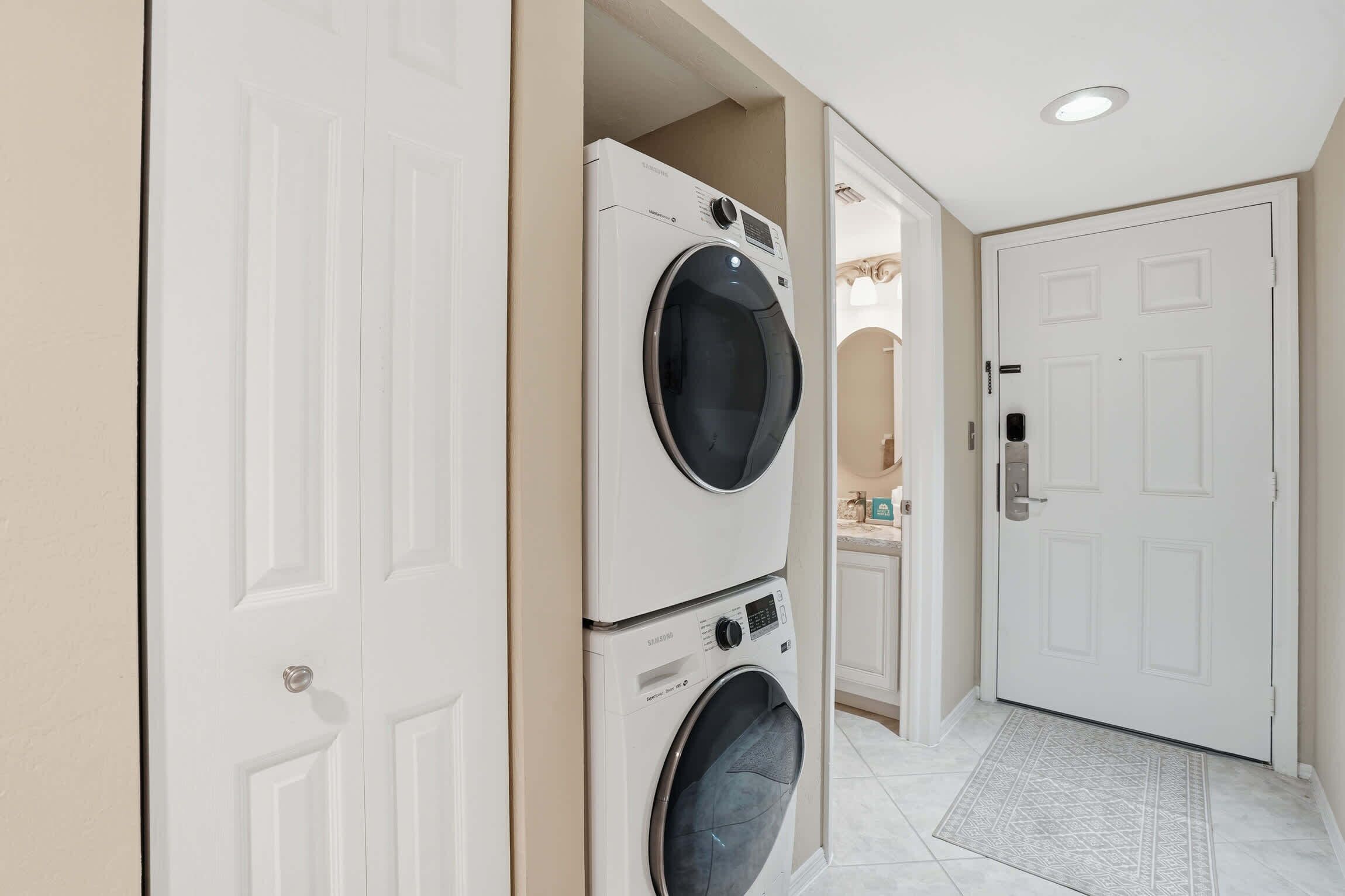 A laundry room with stacked washers and dryers, a white door, and a tiled floor.