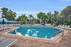 A rectangular swimming pool with a clear blue water surface, surrounded by a tiled deck with lounge chairs and umbrellas. - G-144 - First Floor - End Unit With Lake Views! (Naples)