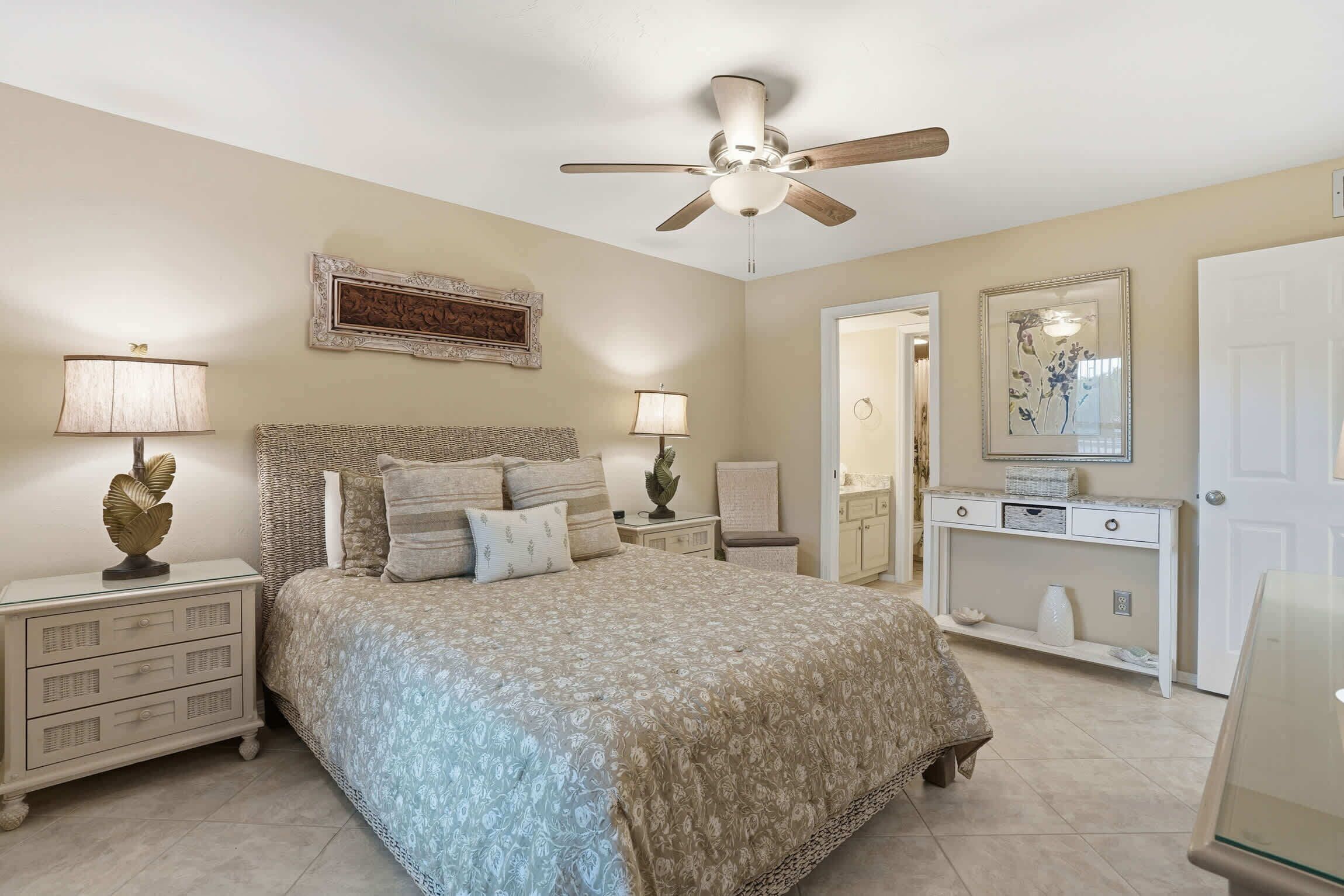 A bedroom with a bed, nightstands, a dresser, a ceiling fan, and a door.