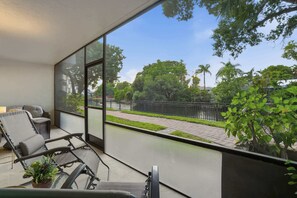 A balcony with a view of a tree-lined street and a black fence. - G-144 - First Floor - End Unit With Lake Views! (Naples)